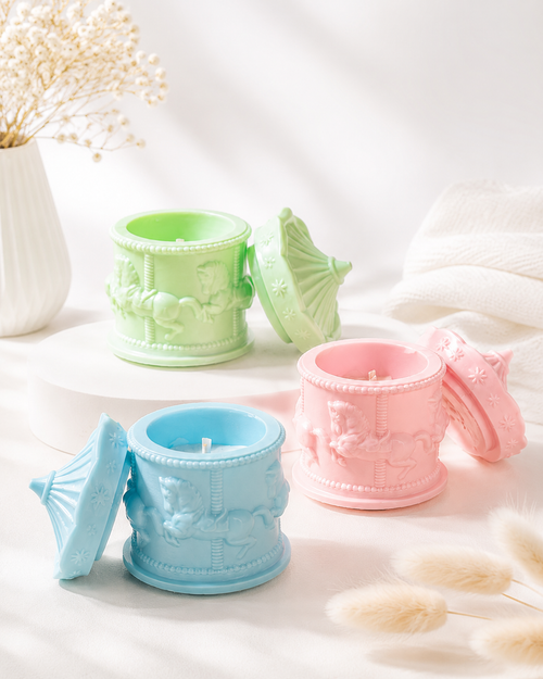 Three embossed wax melts in decorative cup-shaped containers, shown in pastel green, light blue, and soft pink, each with its matching lid leaning beside it on a bright white surface.