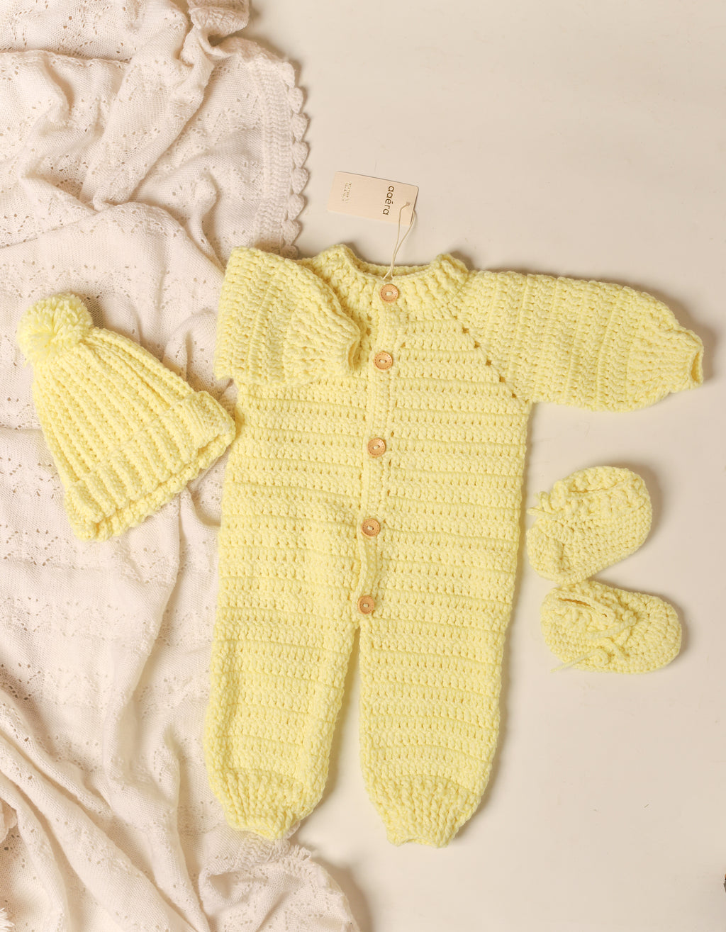 Yellow knitted baby outfit with hat and booties on a beige background