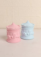 Two pastel-colored carousel-themed jars on a beige background