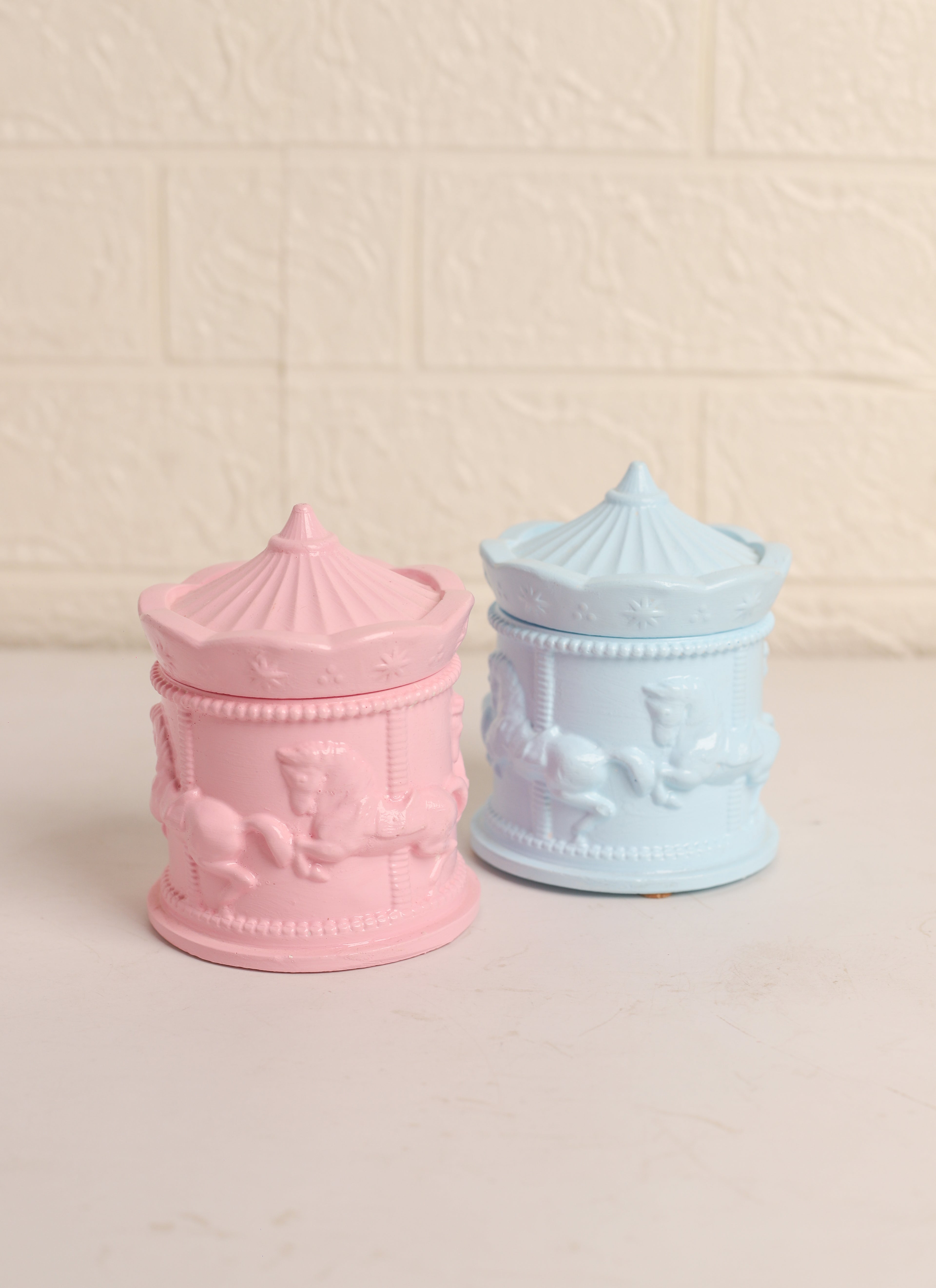 Two pastel-colored carousel-themed jars on a beige background